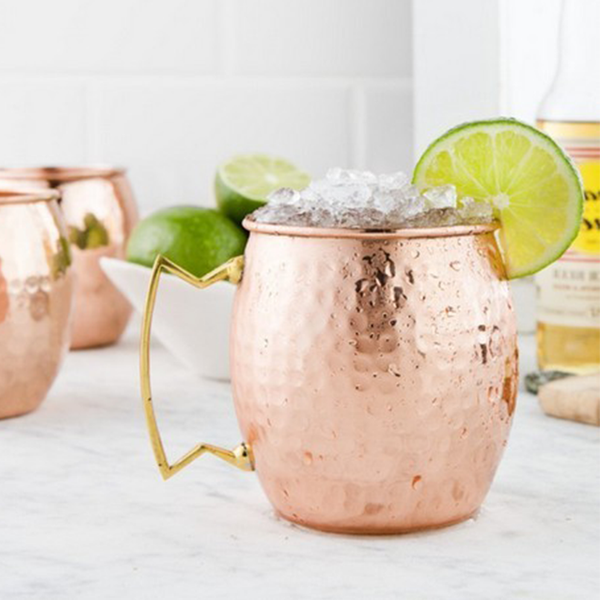 three Moscow Muled copper mugs with one mug filled with crush ice and citrus slice wedged on its rim