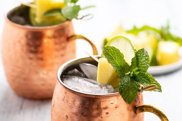 two Moscow Muled copper mugs filled with liquid, ice, sliced lime and mint leaves