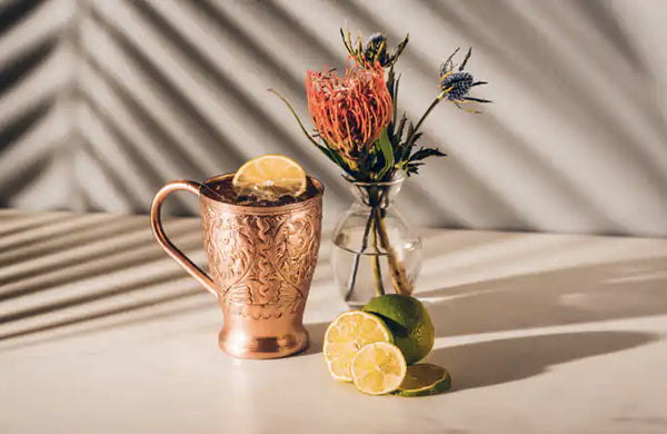 decorative copper mug filled with liquid ice and citrus slice beside a clear glass vase with flowers