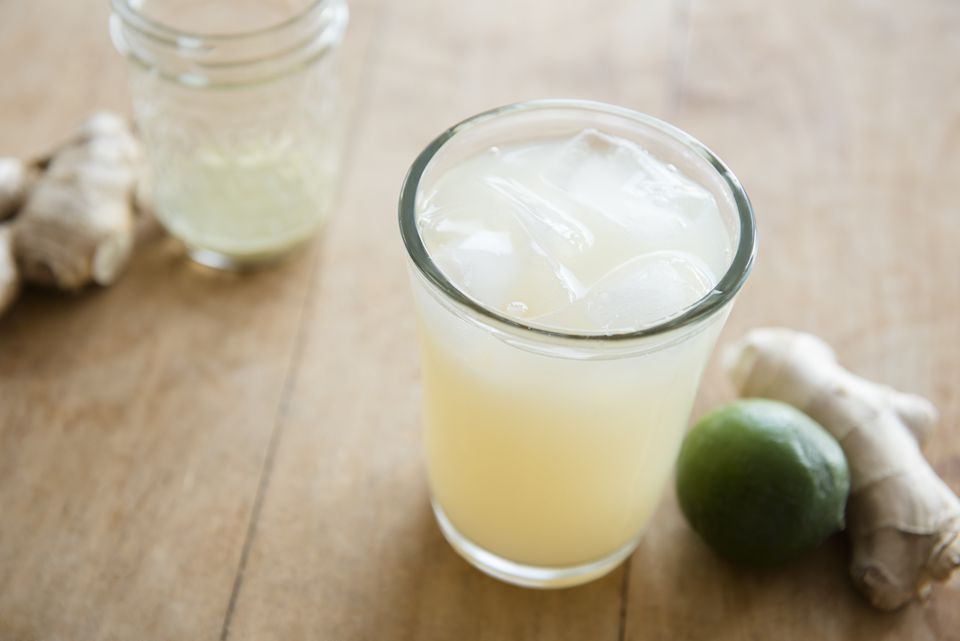 glass filled with ginger brew placed on a wooden table beside a ginger and lime