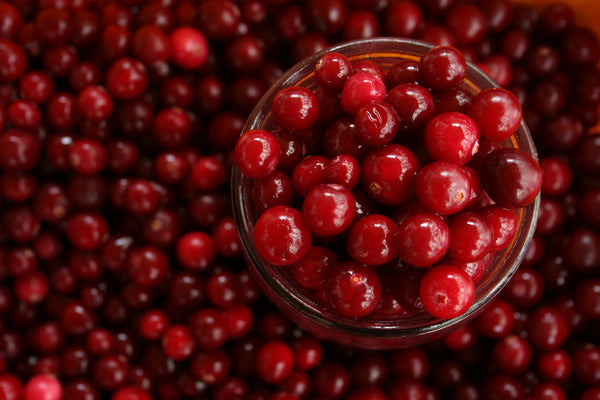 many pieces of cranberries and glass jar full of cranberries on the right side