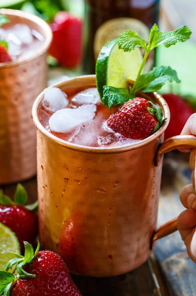 two copper mugs filled with liquid ice strawberry sliced citrus and herb
