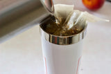 A person pours boiling water into a travel mug containing two tea bags.