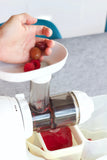 A person puts a handful of raspberries and grapes into a juicer. 