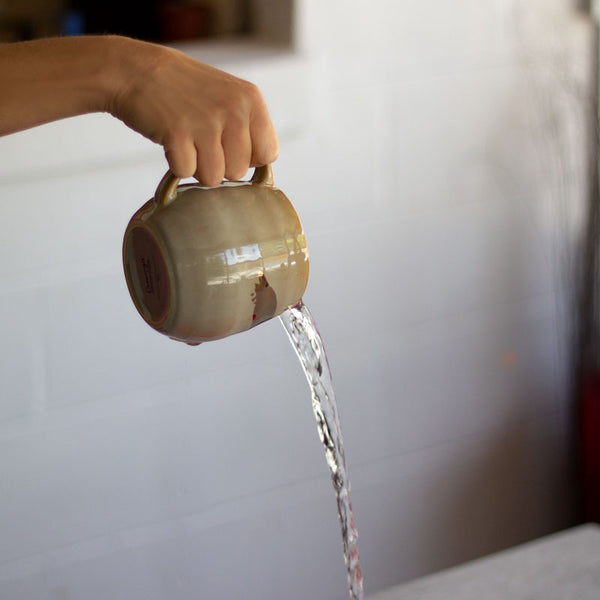 A person pours out a mug of hot water into a sink. 