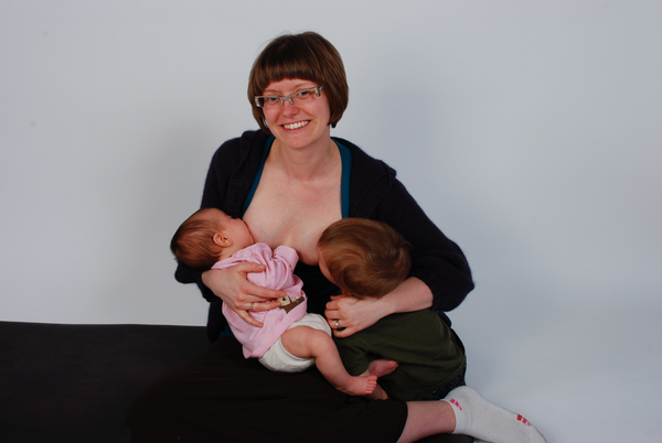 Smiling mother breastfeeding two children at once