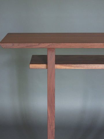 A walnut console table has a lovely arching grain pattern at the top of the table leg, perfectly balanced with the sweeping grain pattern of the table top and shelf.