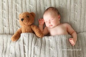 Baby liegt neben Teddybär und schläft