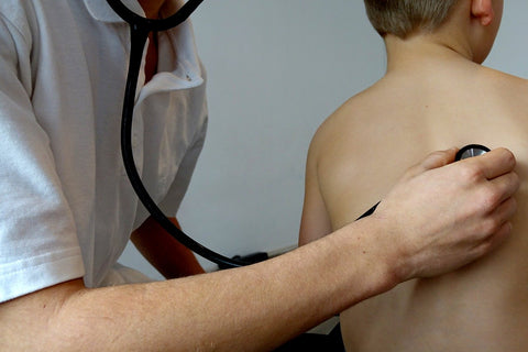 Kinderarzt horcht Kind mit einem Stethoskop am Rücken ab