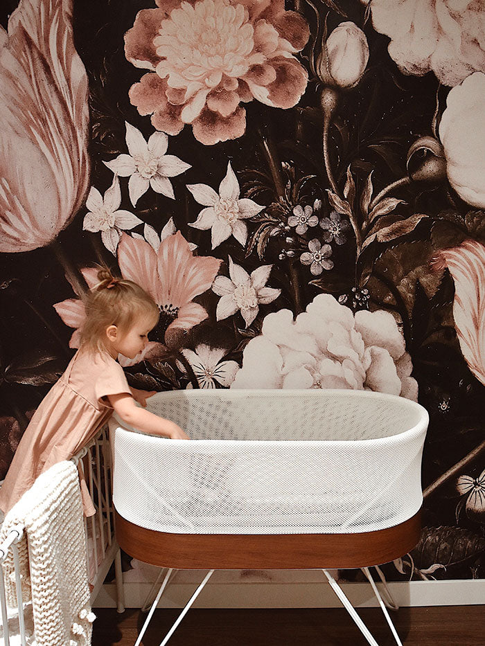 big sister visiting baby sister’s nursery with flower wallpaper and SNOO bassinet