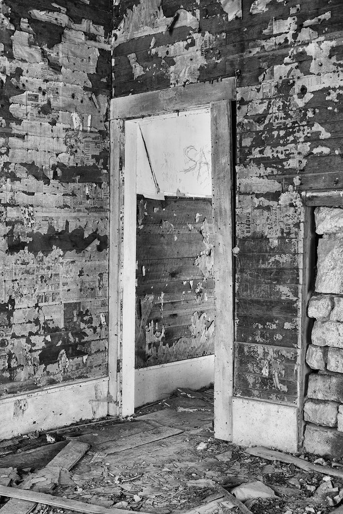 Interior photograph of the abandoned farmhouse. Notice the scraps of newspaper and wallpaper on the walls. Black and white photo by Keith Dotson.