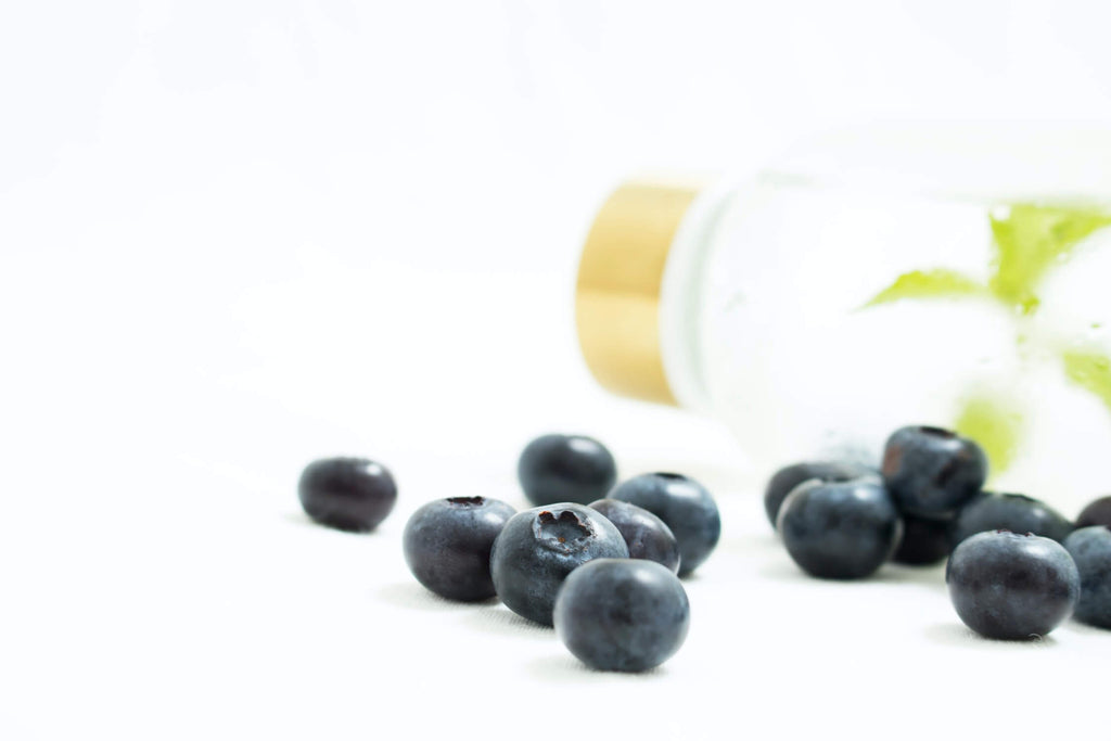pieces of blueberries clear glass bottle behind white background