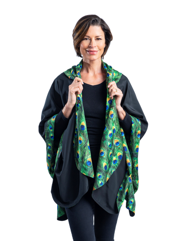 Woman wearing a reversible rain cape which is black on the outside and features a green peacock print reverse