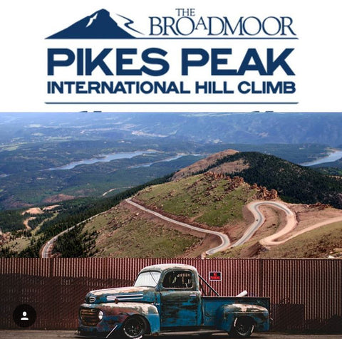 Chuckles Garage's 1949 F1 Farm Truck sits in profile in front of a graphic of the sprawling Pike's Peak track under a graphic for the Pike's Peak logo.