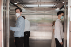 4 people wearing masks in an elevator, each in a corner practicing social distancing. 