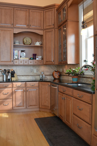Natural lighting shines through the window in front of the kitchen sink, featuring an anti-fatigue mat.