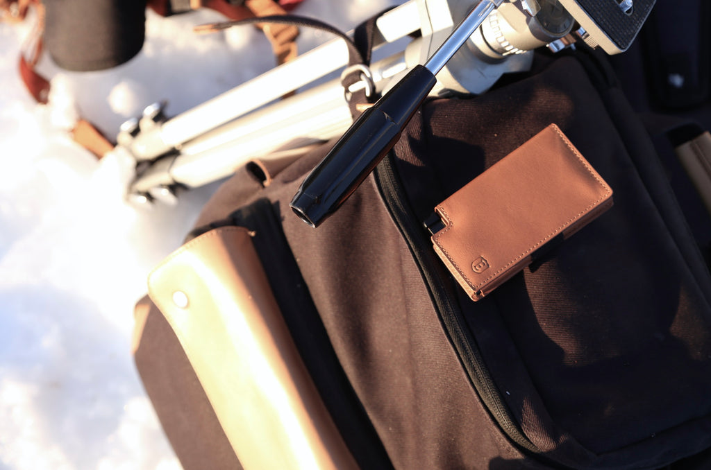 Image of a tan smart wallet placed on a snowmobile amidst the slopes.