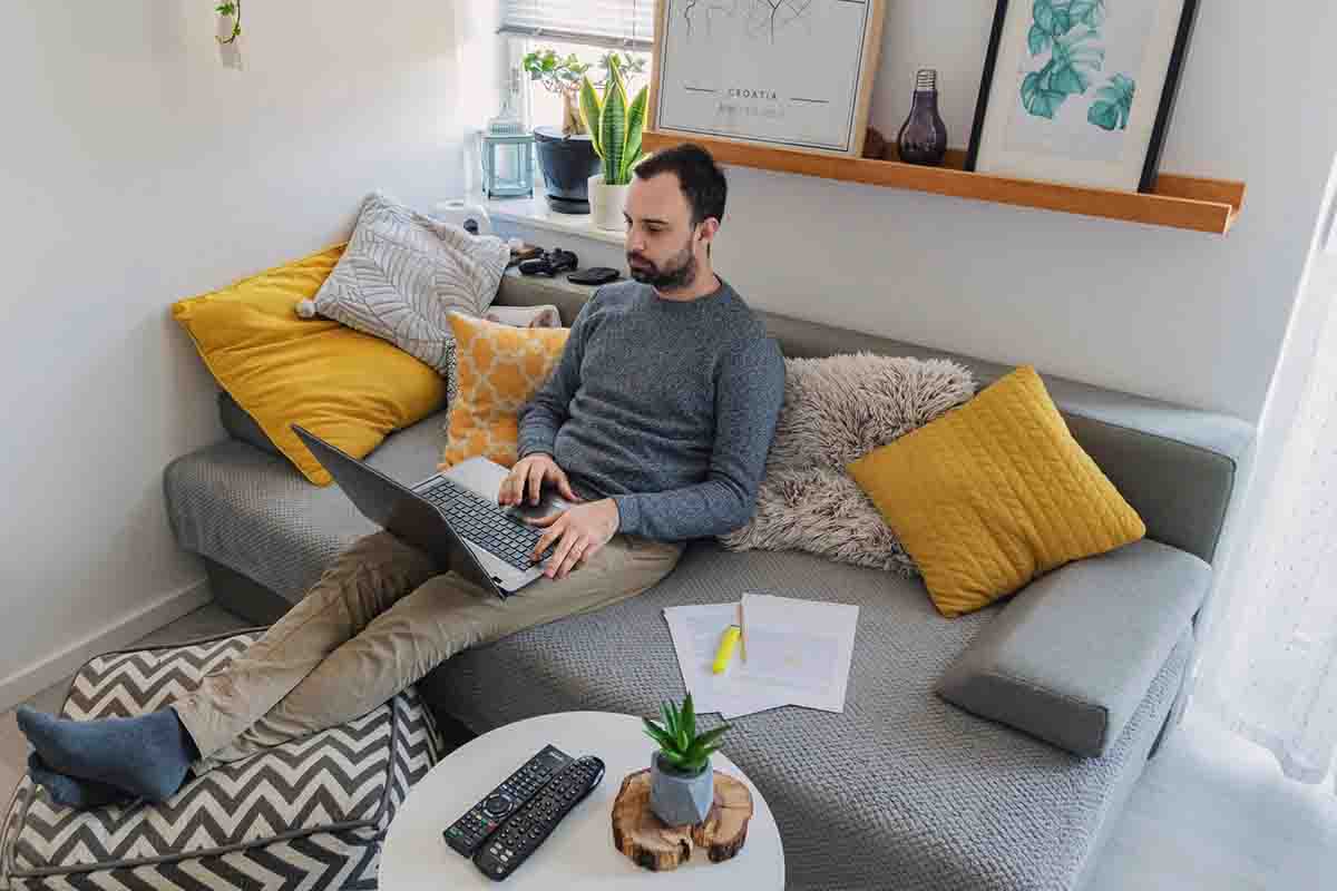 Man sitting on couch with legs on ottoman working on laptop computer
