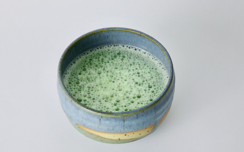 tea ceremony preparation of matcha green tea, super frothy in a blue bowl, white countertop