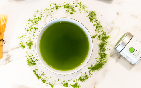 bowl of matcha green tea on a granite countertop, with a circle of matcha stylized around it, and a bamboo whisk