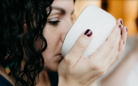 woman with painted fingernails drinking and slurping matcha green tea from a white bowl with a blurred background