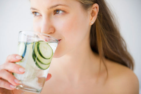 a woman drinking water with cucumbers in it