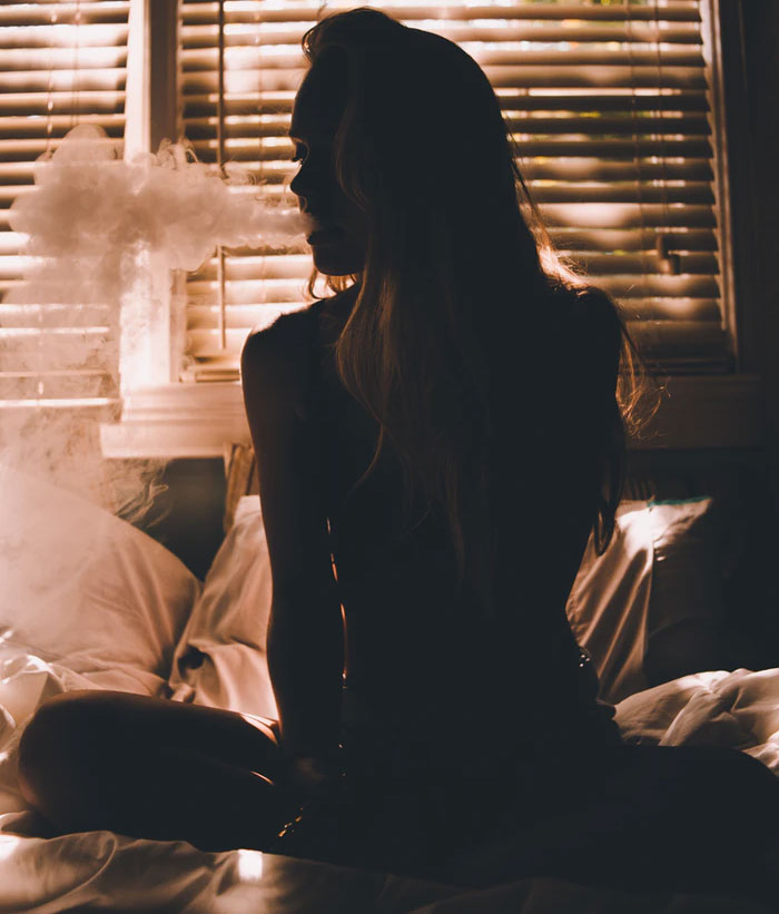 A woman sits cross-legged in bed smoking