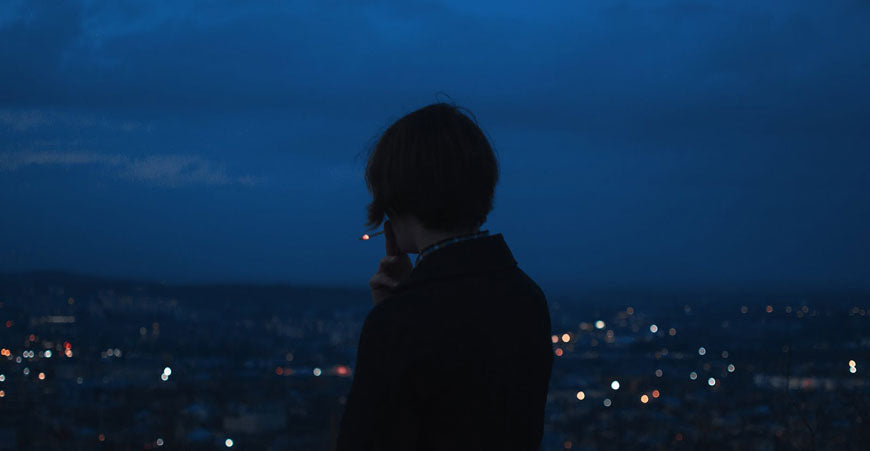 Rear view of man smoking 2 hitter pipe while overlooking a city at night