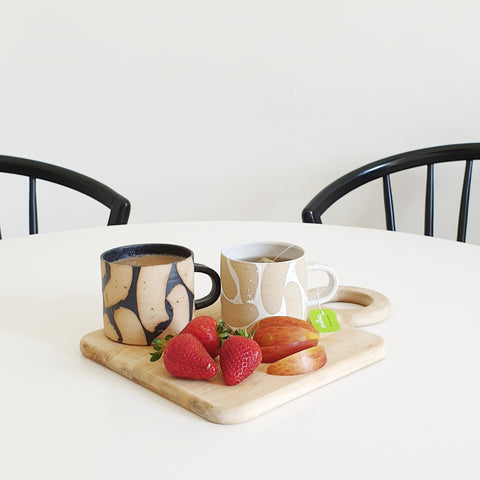 two hand made mugs sit on a tray with fruit