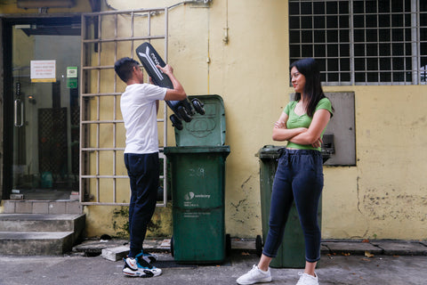 a boy tries to throw a non-certified e-scooter into the rubbish bin, while a girl looks on disapprovingly