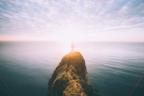 Man standing on cliff overlooking the ocean at sunset