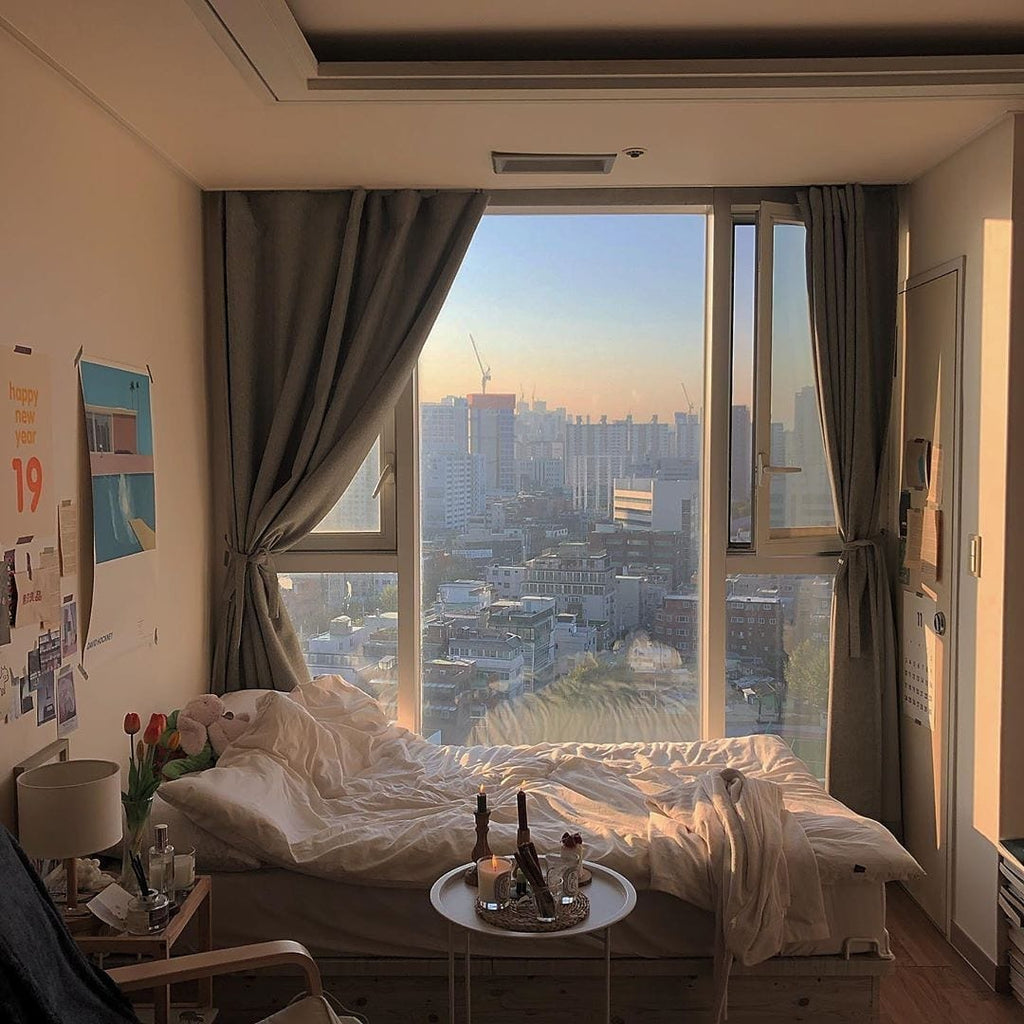 Bedroom with large window and grey curtains overlooking a cityscape.