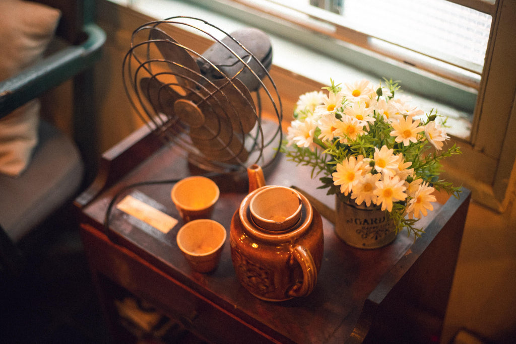 night stand with fan, vase with daisies and teapot with two teacups