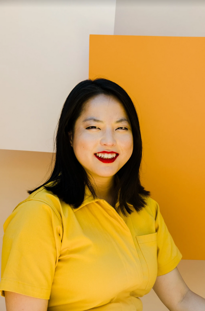 Woman weating a yellow fress sitting in front if a mustard background