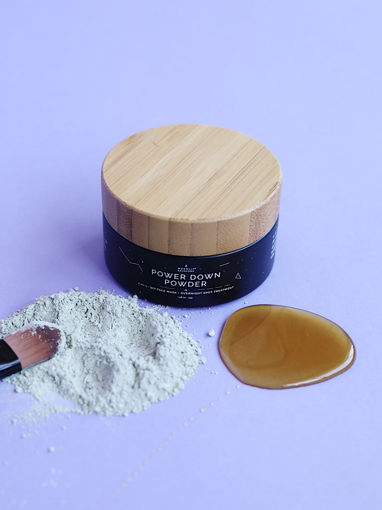 Moonlit Skincare's Power Down Powder with the mask ingredients laying in front of the  container.