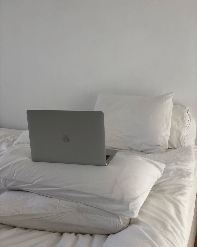 Apple Macbook sitting on pillows of a bed with white bed sheets.