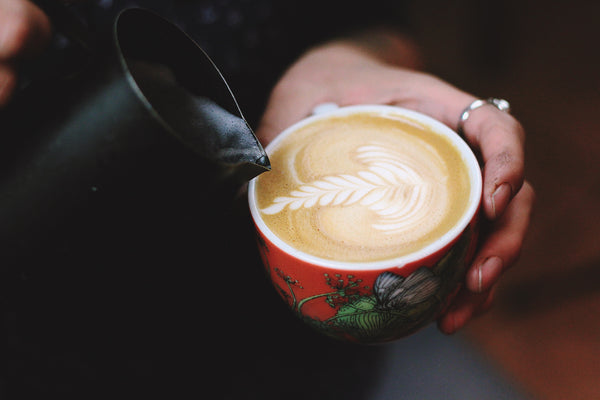 milk being poured into latte in ceramic mug