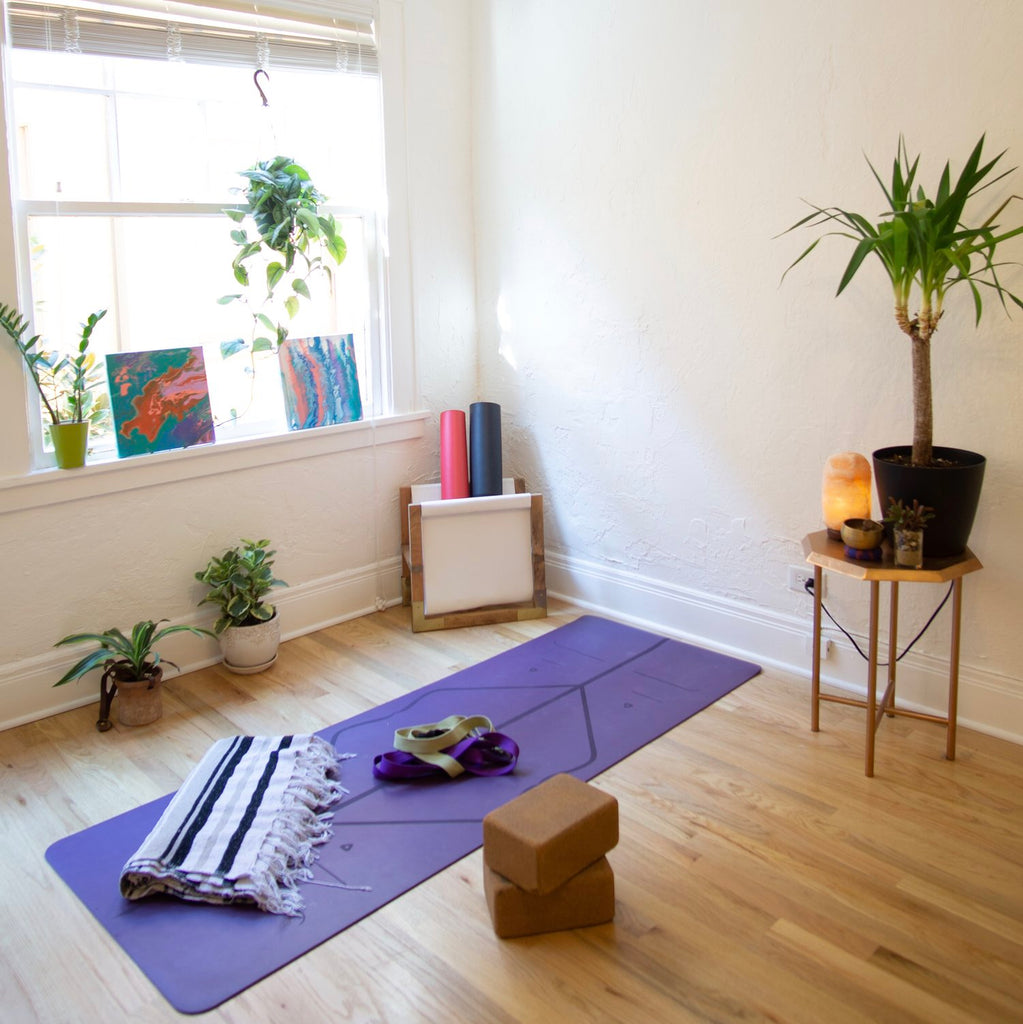 Room with personal home yoga set up that includes: purple yoga mat, brown yoga blocks, and blanket.