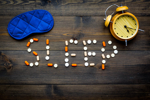 The word "sleep" written out in pills with a sleep mask and an alarm clock.