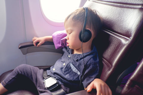 tiny child flying on an airplane. He's sleeping in the seat with headphones on.