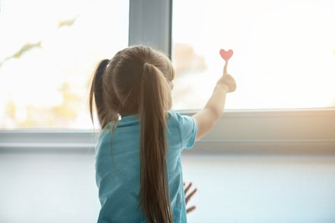 young girl touching heart on window.