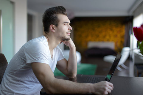 photo of a man sitting in front of a laptop staring in the distance.