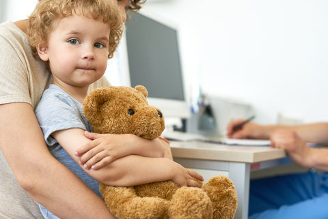 photo of a little boy sitting in parent's lap clutching a teddy bear.