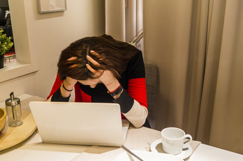 photo of a woman holding head in front of laptop.