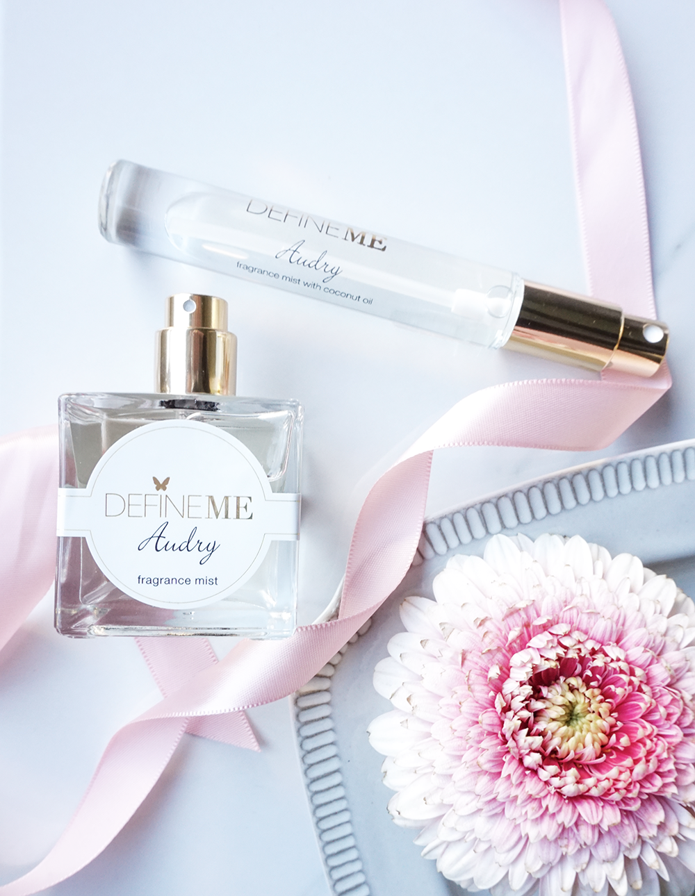 DefineMe Fragrance Audry Mist and purse spray lying on white background with pink ribbon and soft pink flower.