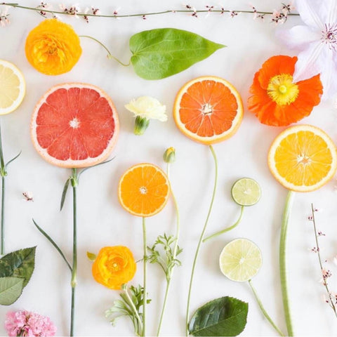 Sliced oranges and blood oranges on white table with leaves and flowers.