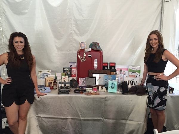 Two ladies standing either side of table with merchandise at MTV's VMA Official Celeb Gift Bag event.