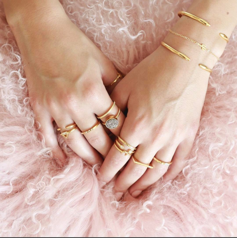 Two hands lying on pink tutu with bracelets and rings on fingers.