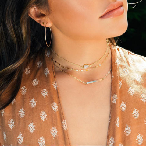 Woman wearing floral top with layered necklaces and hoop earrings.