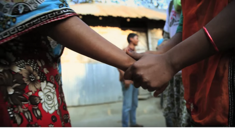 Two people holding hands with man standing in background.